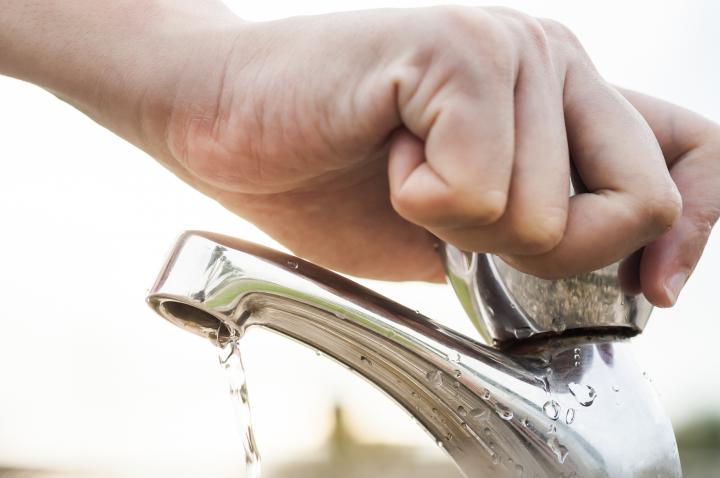 Image of a hand turning off a dripping tap with sunshine in the background.