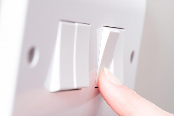Image of a finger pressing a light switch on a wall.