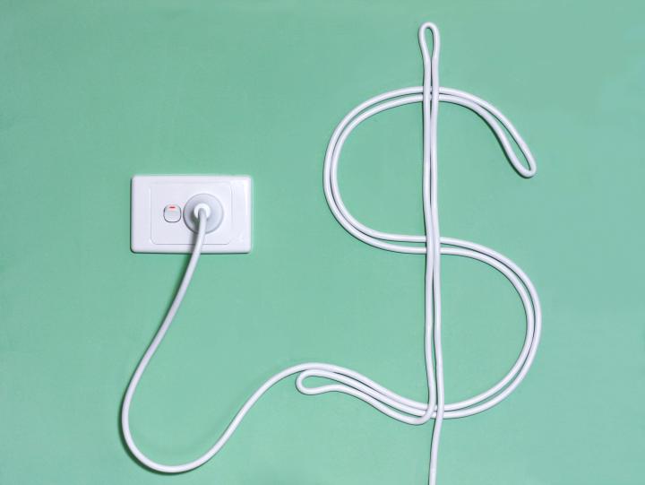 An image showing a wall socket with a power cord plugged in, in the shape of a in the dollar sign