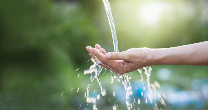 An image of an outstretched hand with water pouring into it, in an outdoor setting. 
