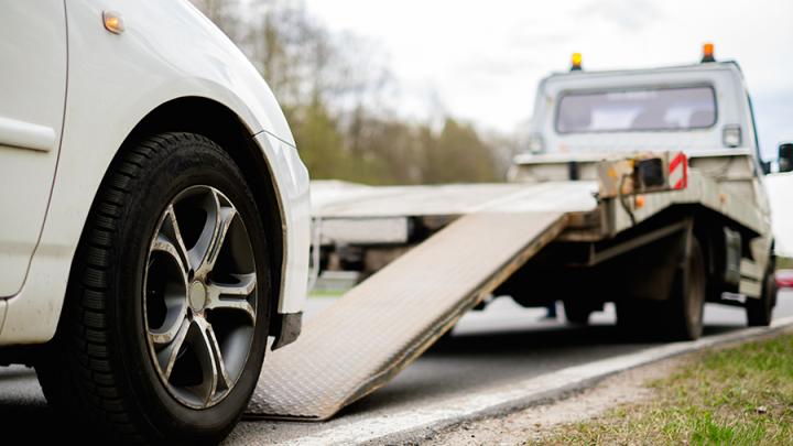 A tow truck in the process of rolling a broken-down car up ramps on to the truck's tray.