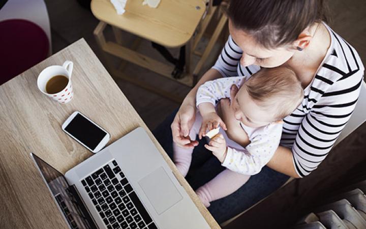 Woman holding baby, looking at laptop