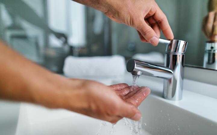 A photo showing a person's hand turning on a bathroom tap, and the person's other handing catching watching coming out of the tap.