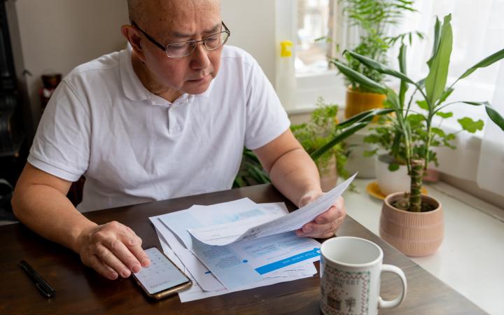 A senior man sitting at a table, looking at a bill, using a calculator.