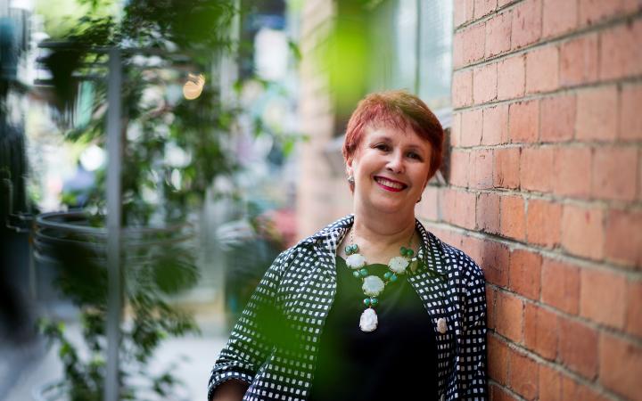 Ann, a water team member at the commission, leans against a brick wall in a Melbourne laneway and smiles at the camera. 