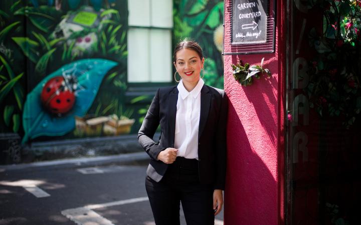 Helena, transport team member at the Essential Services Commission, standing in an artfully graffiti-covered city laneway and smiling at the camera.